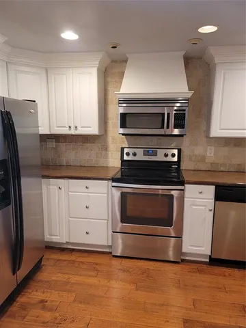 a kitchen with stainless steel appliances granite countertop a refrigerator a sink dishwasher a stove top oven a dining table and chairs with wooden floor