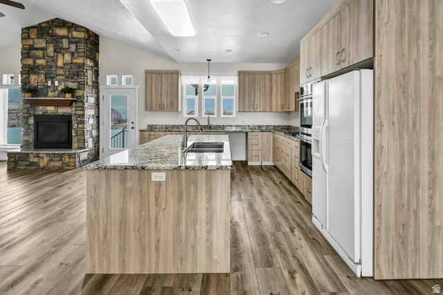 1103 North Brooklyn Road Monroe, UT 84754 - Photo 11 of 78 Kitchen featuring white refrigerator with ice dispenser, light stone counters, light brown cabinets, a fireplace, and vaulted ceiling
