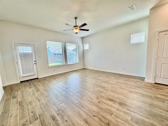 an empty room with wooden floor chandelier fan and windows