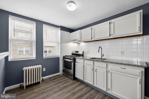 a kitchen with granite countertop a stove a sink and white cabinets