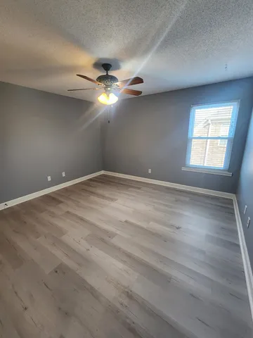 an empty room with wooden floor fan and windows
