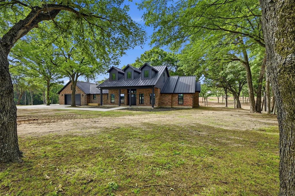 410 Arkansas Road Sadler, TX 76264 - Photo 1 of 40 Brick-clad residence featuring a dark metal roof, multiple dormer windows, a covered front entry, and an attached two-car garage