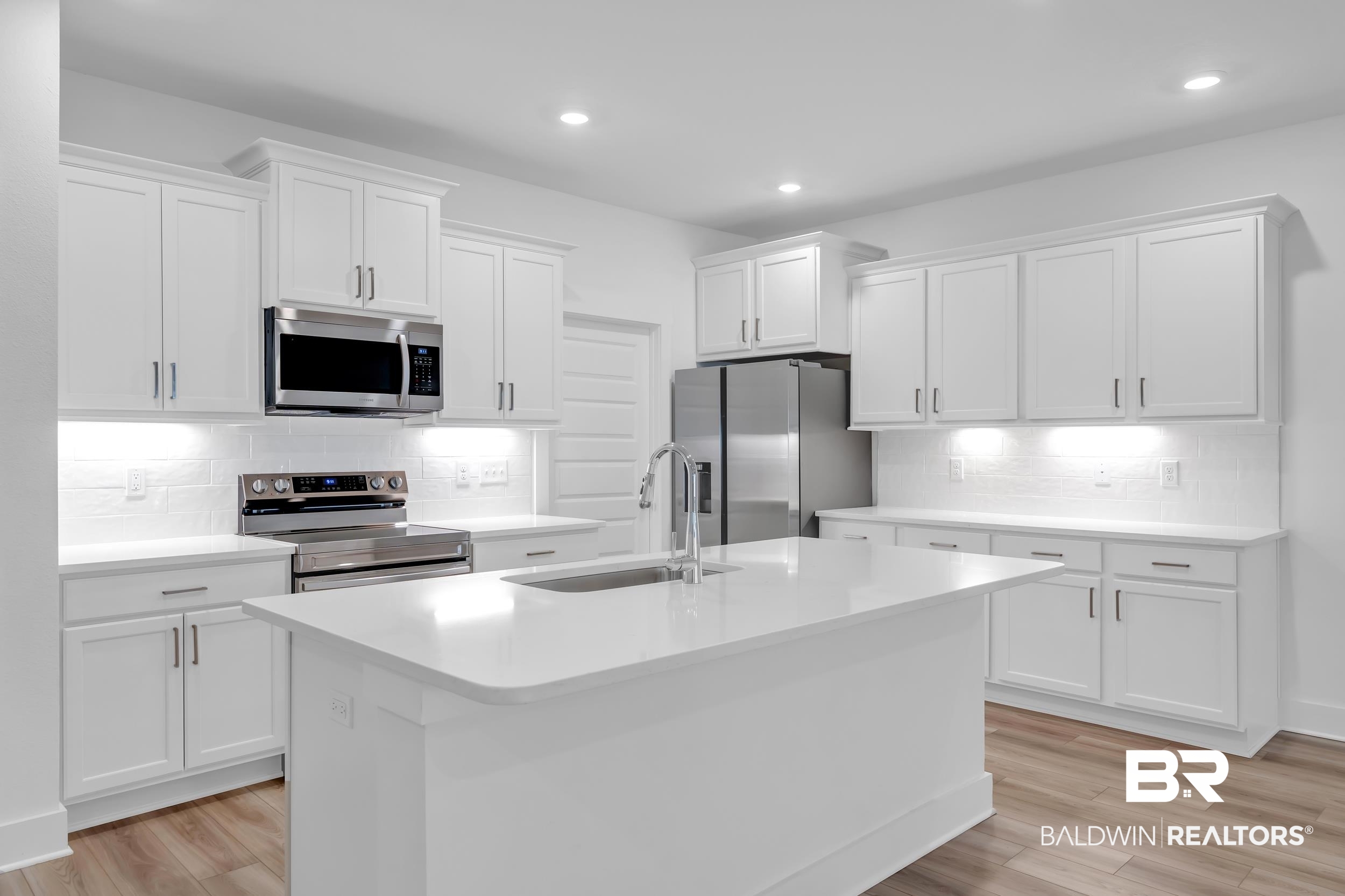 9933 Weller Cove Foley, AL 36535 - Photo 9 of 36 Modern kitchen featuring a central island with an undermount sink, white cabinetry with contemporary hardware, stainless steel appliances, a white subway tile backsplash, and wood-finish flooring