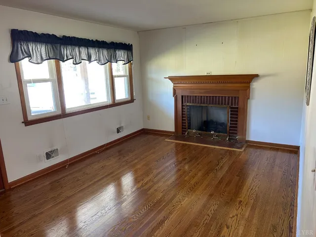 an empty room with wooden floor fireplace and windows