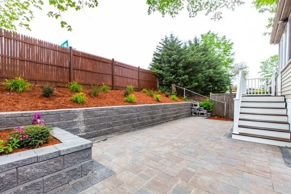 a view of a white house with a small yard and large wooden fence and a large tree