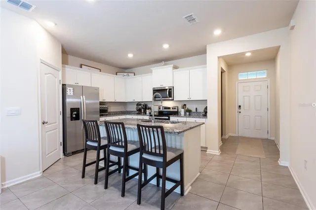 a kitchen with stainless steel appliances granite countertop a refrigerator a sink a stove a dining table and chairs