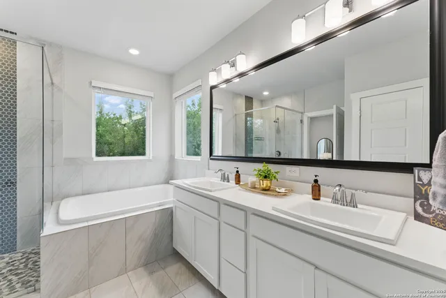 a bathroom with a double vanity sink a large mirror and a bathtub