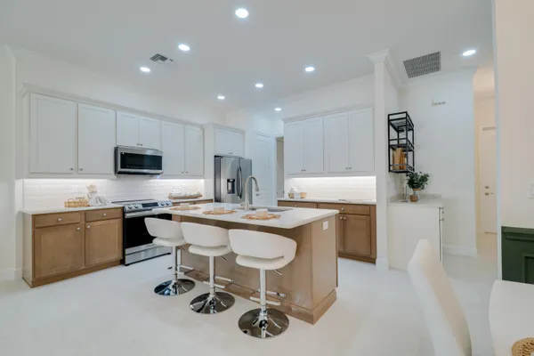 a kitchen with kitchen island granite countertop a sink a stove a refrigerator cabinets and chairs