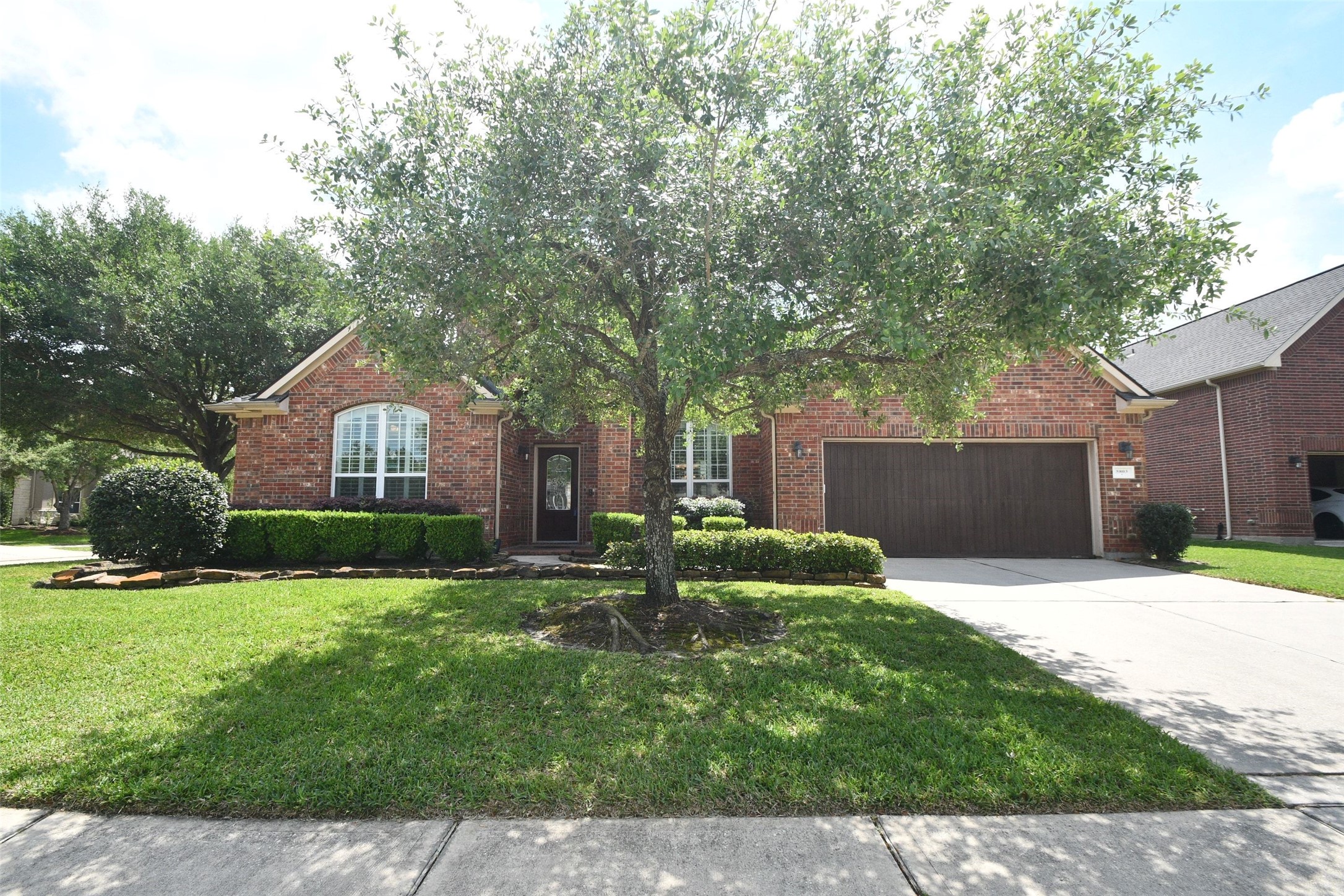 Charming brick home with a well-maintained front yard and mature tree. Features include a double garage, nicely trimmed hedges, and a welcoming entrance path.