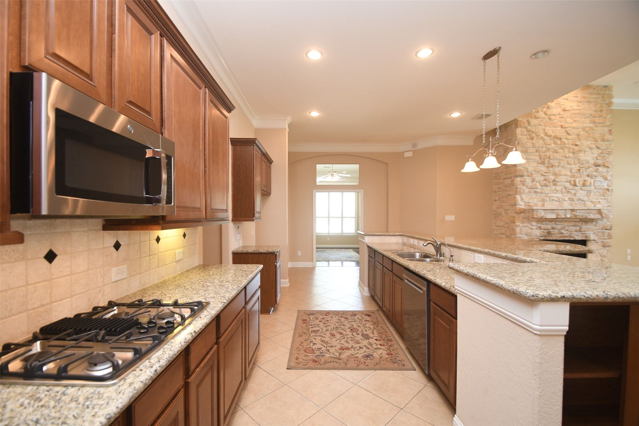 5803 Oakdale Meadows Spring, TX 77379 - Photo 11 of 21 This kitchen features granite countertops, a gas stove, and stainless steel appliances. It has ample wooden cabinetry, a tile backsplash, and an open layout with a view into a bright living space. The neutral tones and pendant lighting add warmth and elegance.