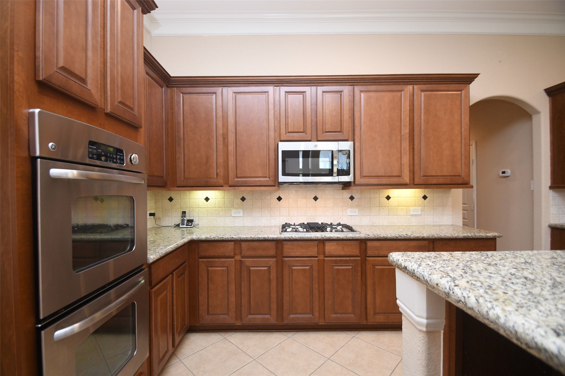 5803 Oakdale Meadows Spring, TX 77379 - Photo 12 of 21 This kitchen features warm wooden cabinetry, granite countertops, and stainless steel appliances, including a built-in oven and microwave. The space is enhanced by a gas cooktop and a tiled backsplash with decorative accents.