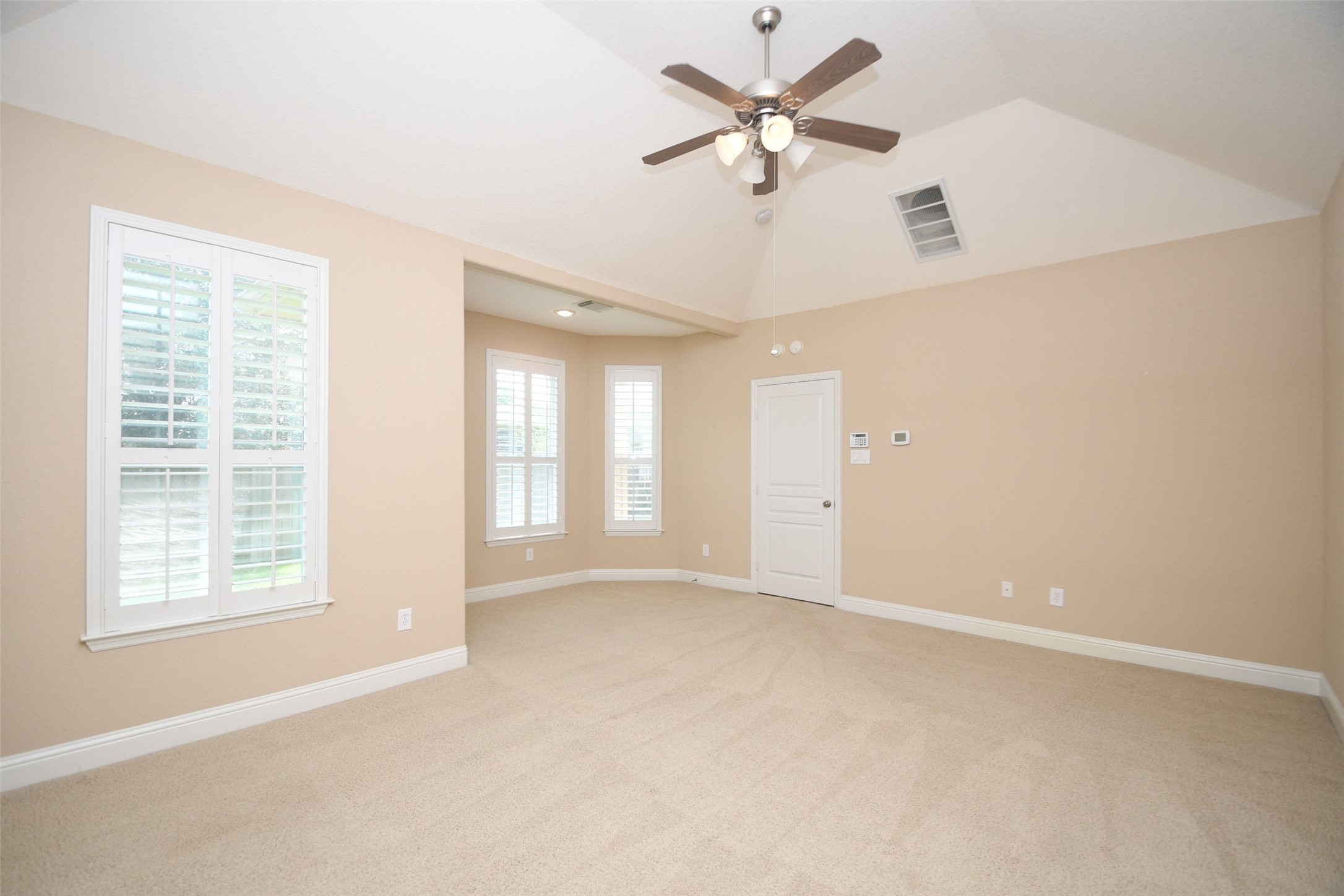 5803 Oakdale Meadows Spring, TX 77379 - Photo 15 of 21 This primary room features a high vaulted ceiling with a ceiling fan, neutral beige walls, and plush carpeting. It has large windows with white shutters allowing natural light, and a central door for easy access. Ideal for a cozy living area or bedroom.