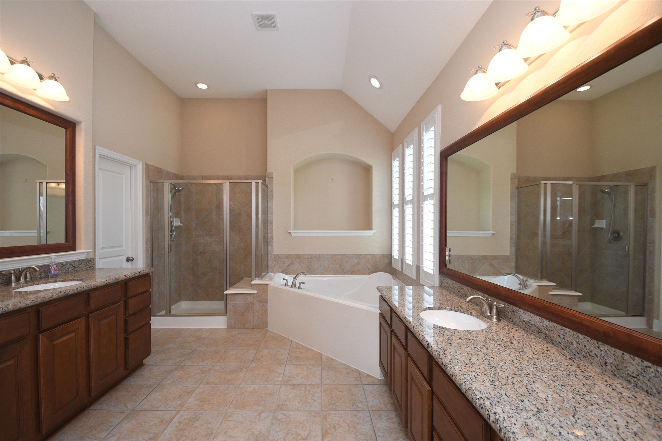 5803 Oakdale Meadows Spring, TX 77379 - Photo 16 of 21 This primary bathroom features dual sinks with granite countertops, a large mirror, a tiled walk-in shower, and a separate soaking tub. The room is bright with natural light from shuttered windows and has ample cabinet storage.