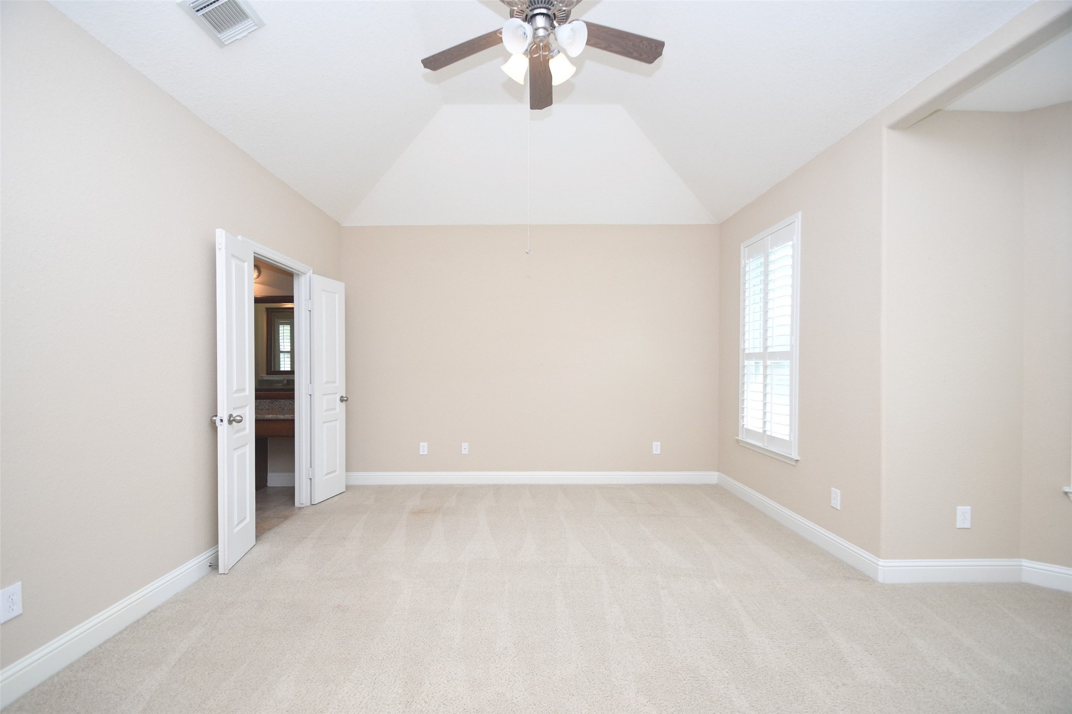 5803 Oakdale Meadows Spring, TX 77379 - Photo 18 of 21 This spacious, light-filled bedroom features neutral walls, plush carpeting, a ceiling fan, and a vaulted ceiling. It includes a large window with shutters and a doorway leading to an en-suite bathroom.
