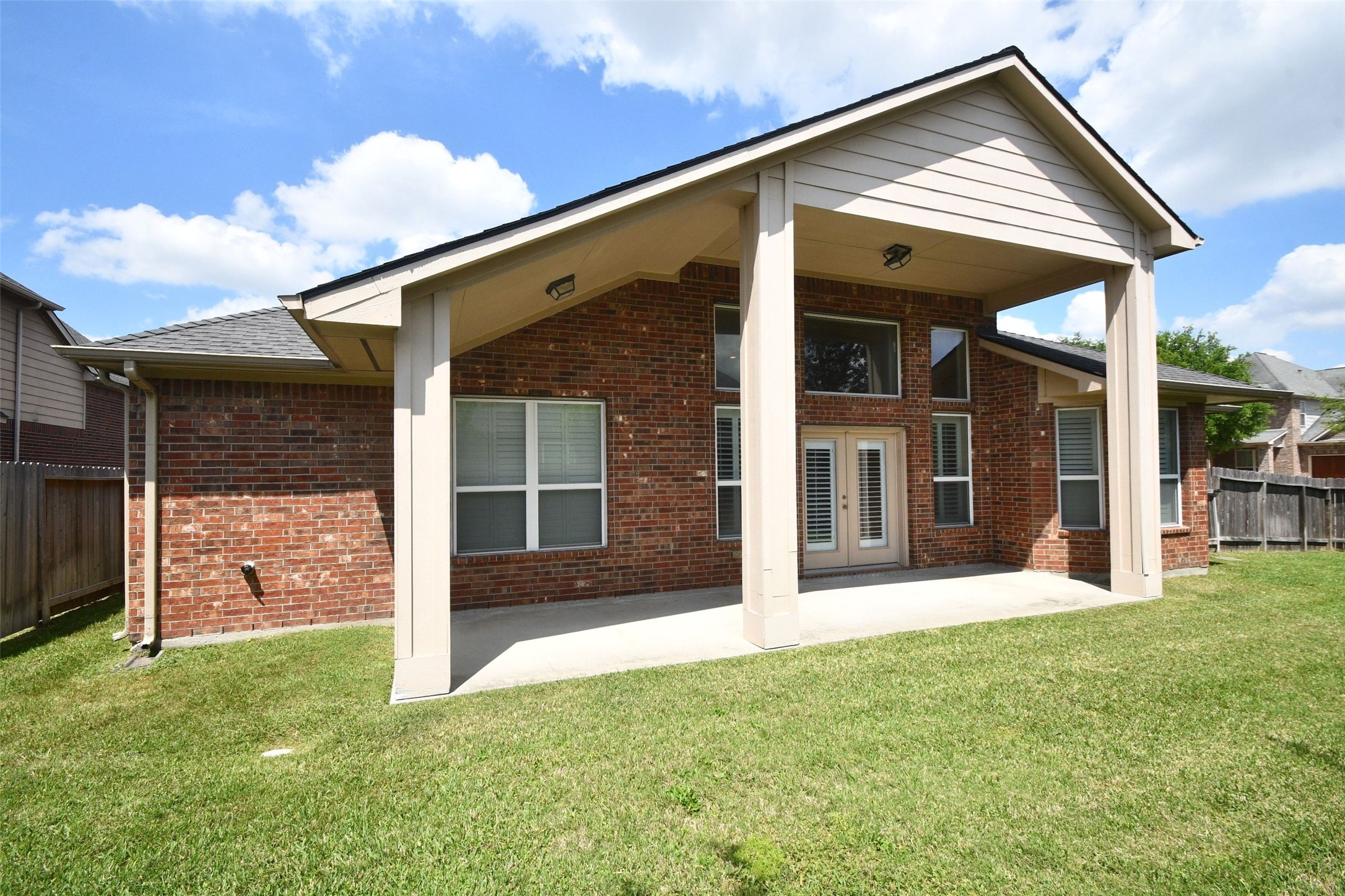 5803 Oakdale Meadows Spring, TX 77379 - Photo 21 of 21 This photo showcases the back of a brick house featuring a covered patio with high ceilings and large windows, overlooking a spacious, well-maintained lawn.