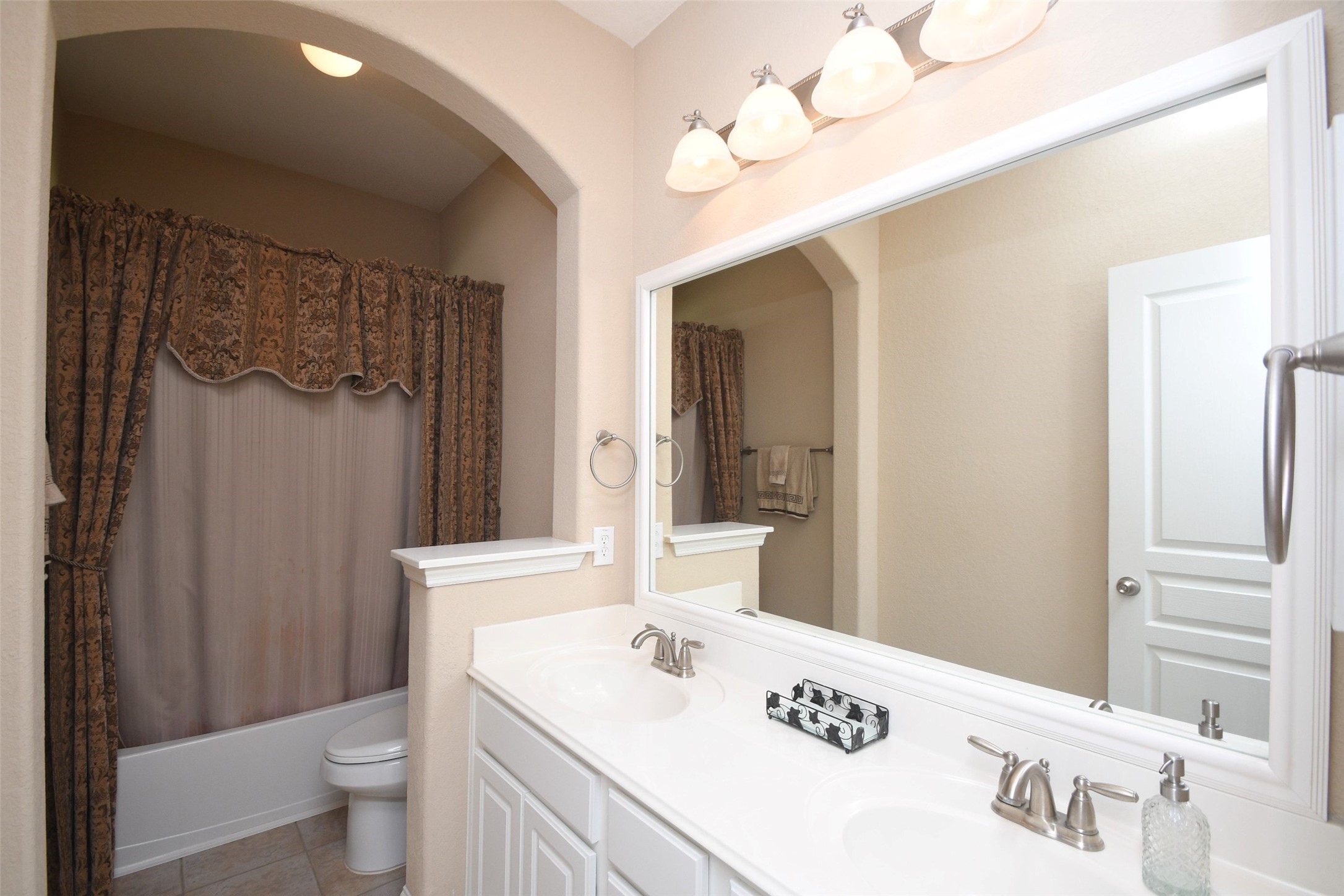 5803 Oakdale Meadows Spring, TX 77379 - Photo 6 of 21 This bathroom features a double-sink vanity with a large mirror, elegant lighting, and neutral tones. It includes a shower-tub combo with decorative curtains and ample lighting, creating a cozy and functional space.