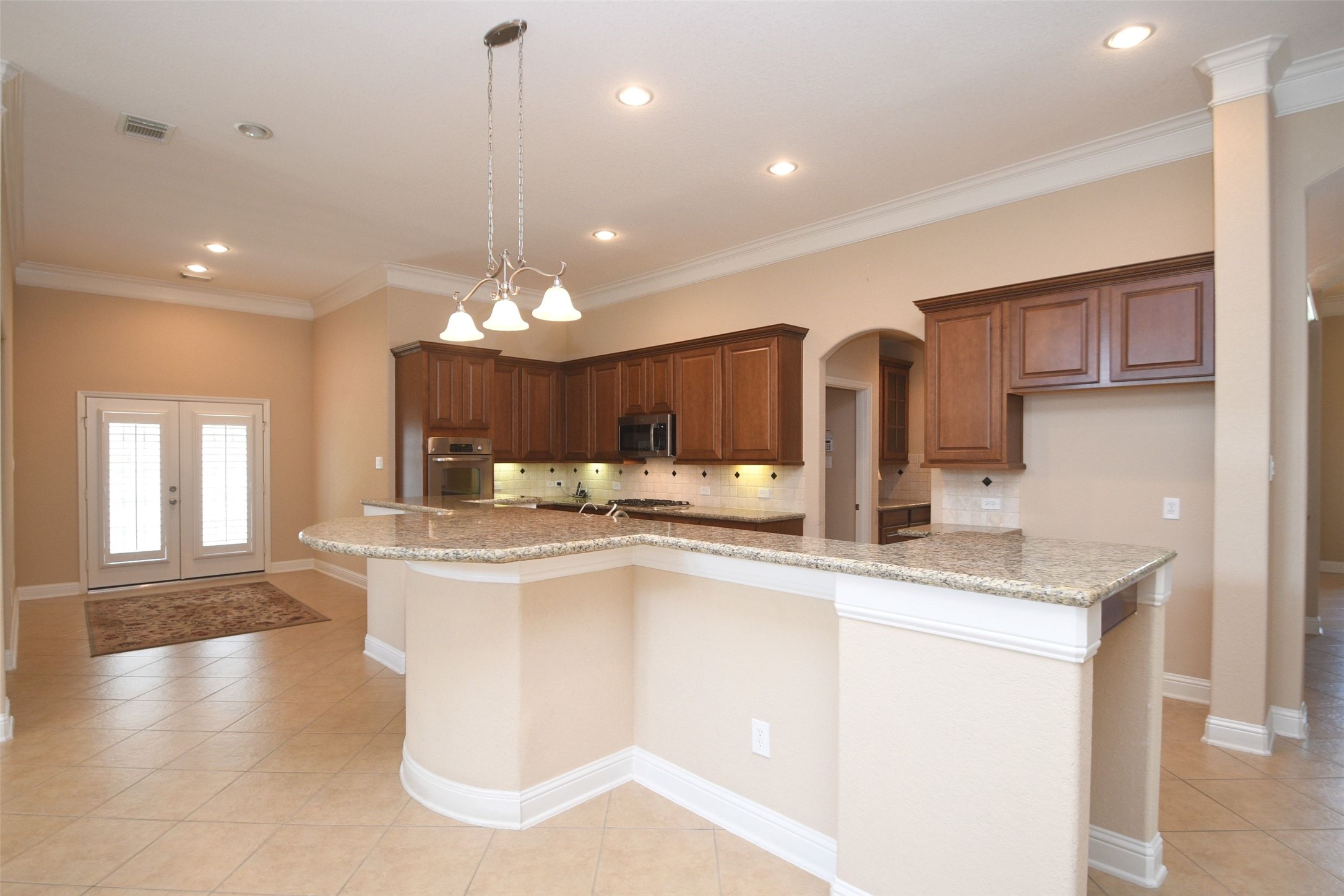 5803 Oakdale Meadows Spring, TX 77379 - Photo 10 of 21 This spacious kitchen features granite countertops, warm wood cabinetry, and modern appliances. It opens into a well-lit dining area with tile flooring and French doors, creating an inviting and functional space.