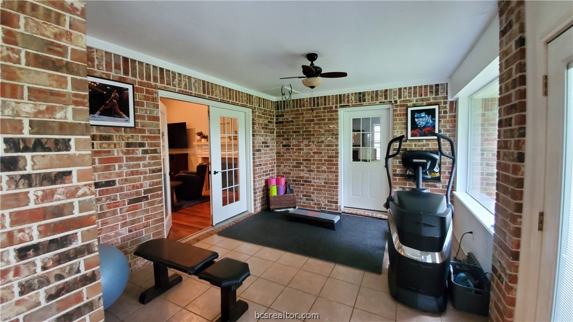 5660 Falling Water Bryan, TX 77808 - Photo 9 of 27 Exercise room with french doors, tile patterned flooring, ceiling fan, and brick wall