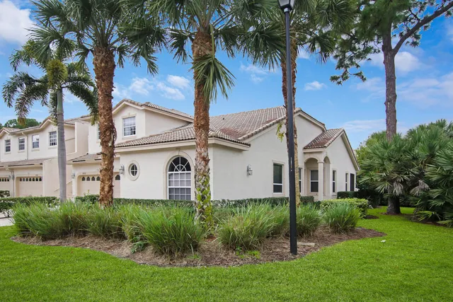 a view of a white house with a big yard and potted plants and palm trees