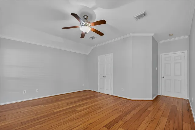 a view of an empty room with wooden floor and a ceiling fan