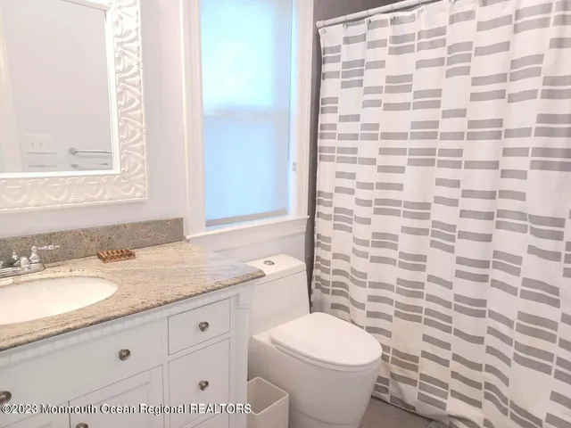 a bathroom with a granite countertop toilet a sink a mirror and shower curtain
