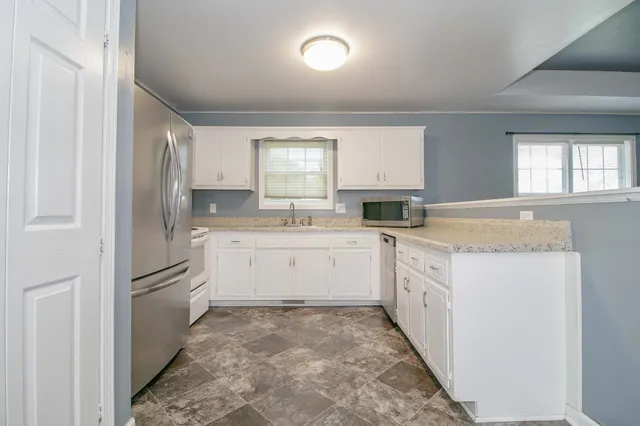 a kitchen with granite countertop a refrigerator and white cabinets