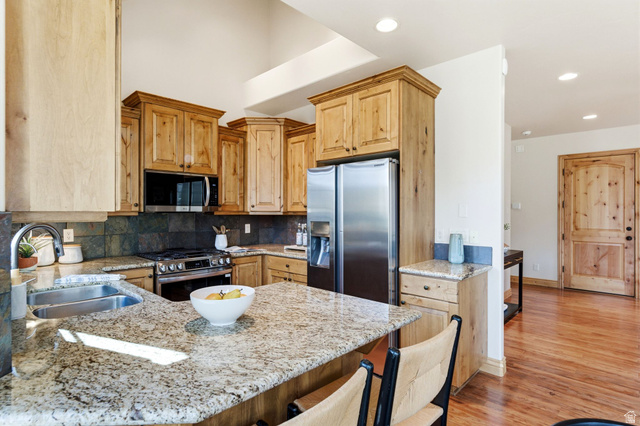 3026 Lower Saddleback Road Park City, UT 84098 - Photo 11 of 71 Kitchen featuring light stone counters, a breakfast bar, appliances with stainless steel finishes, a peninsula, and light wood finished floors