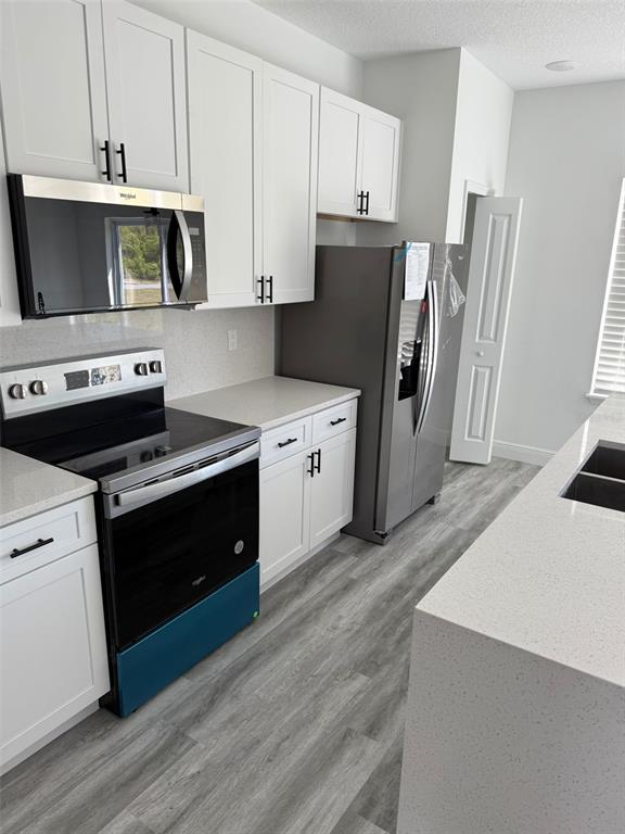 17490 Southwest 27th Circle Ocala, FL 34473 - Photo 4 of 12 a kitchen with stainless steel appliances a stove a microwave a sink a refrigerator white cabinets and wooden floor