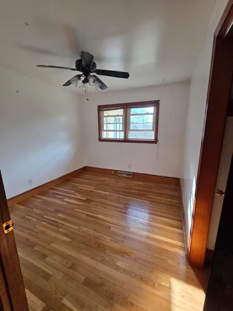 an empty room with wooden floor ceiling fan and windows