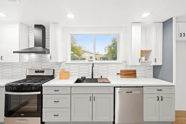 a large kitchen with stainless steel appliances a sink dishwasher a stove and white cabinets with wooden floor