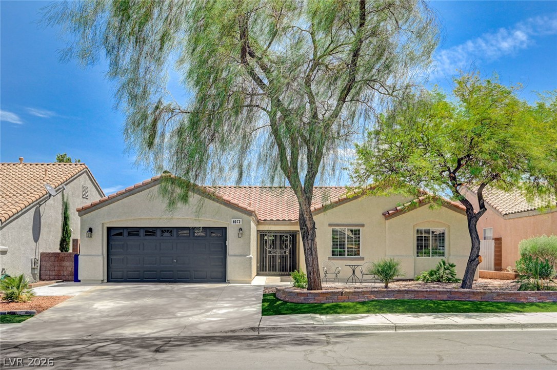 1072 Reed Point Court Henderson, NV 89002 - Photo 1 of 60 A welcoming facade with a garage and a well-tended landscape featuring mature trees and a brick-lined bed.