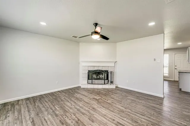 a view of an empty room with wooden floor fireplace and a window