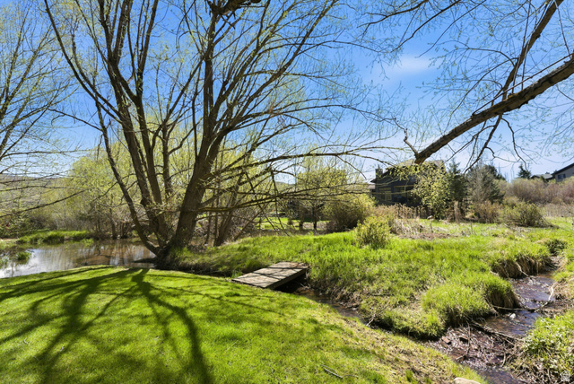 7935 Mustang Loop Road Park City, UT 84098 - Photo 18 of 60 Expansive natural landscape featuring a pond, a wooden footbridge, a mature tree, a grassy lawn, and a stream