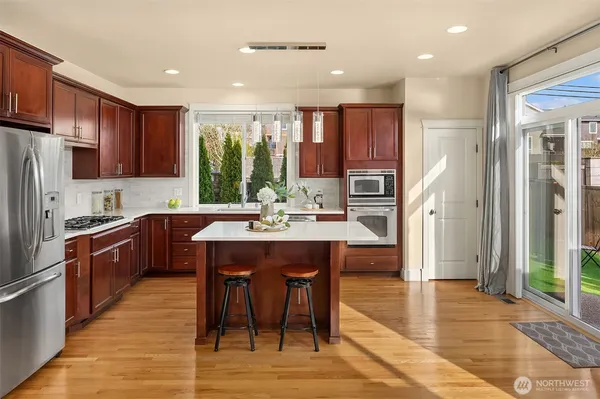 a kitchen with stainless steel appliances a sink a stove a refrigerator cabinets and a dining table with wooden floor
