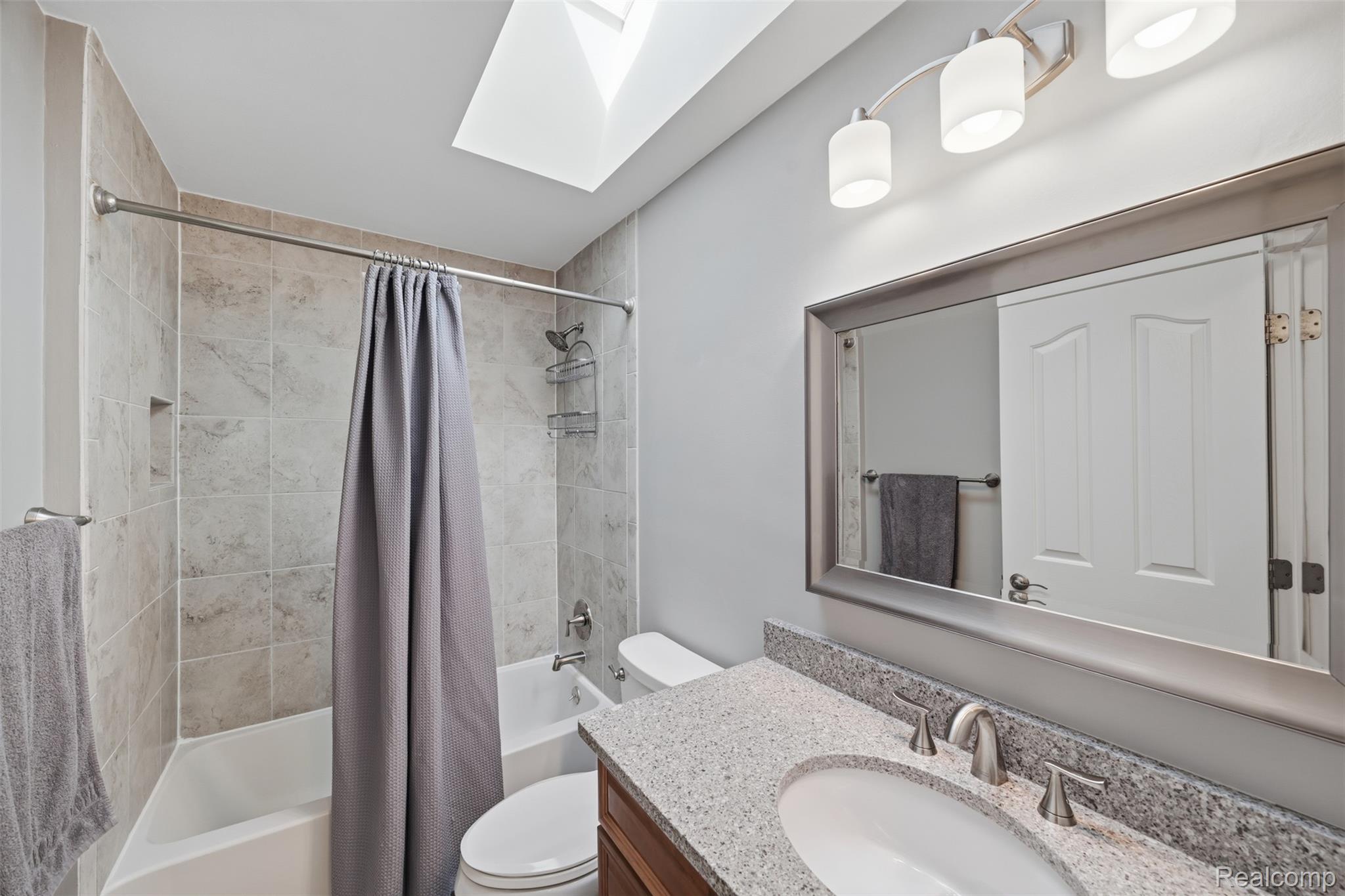 1087 Collingwood Drive Rochester, MI 48307 - Photo 42 of 56 Bathroom featuring a skylight, tile-surround bathtub, vanity with a stone countertop, and a framed mirror