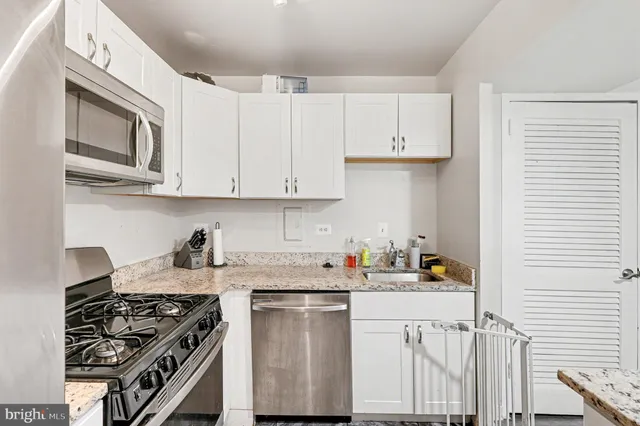 a kitchen with stainless steel appliances granite countertop a stove a sink dishwasher and a microwave oven with white cabinets