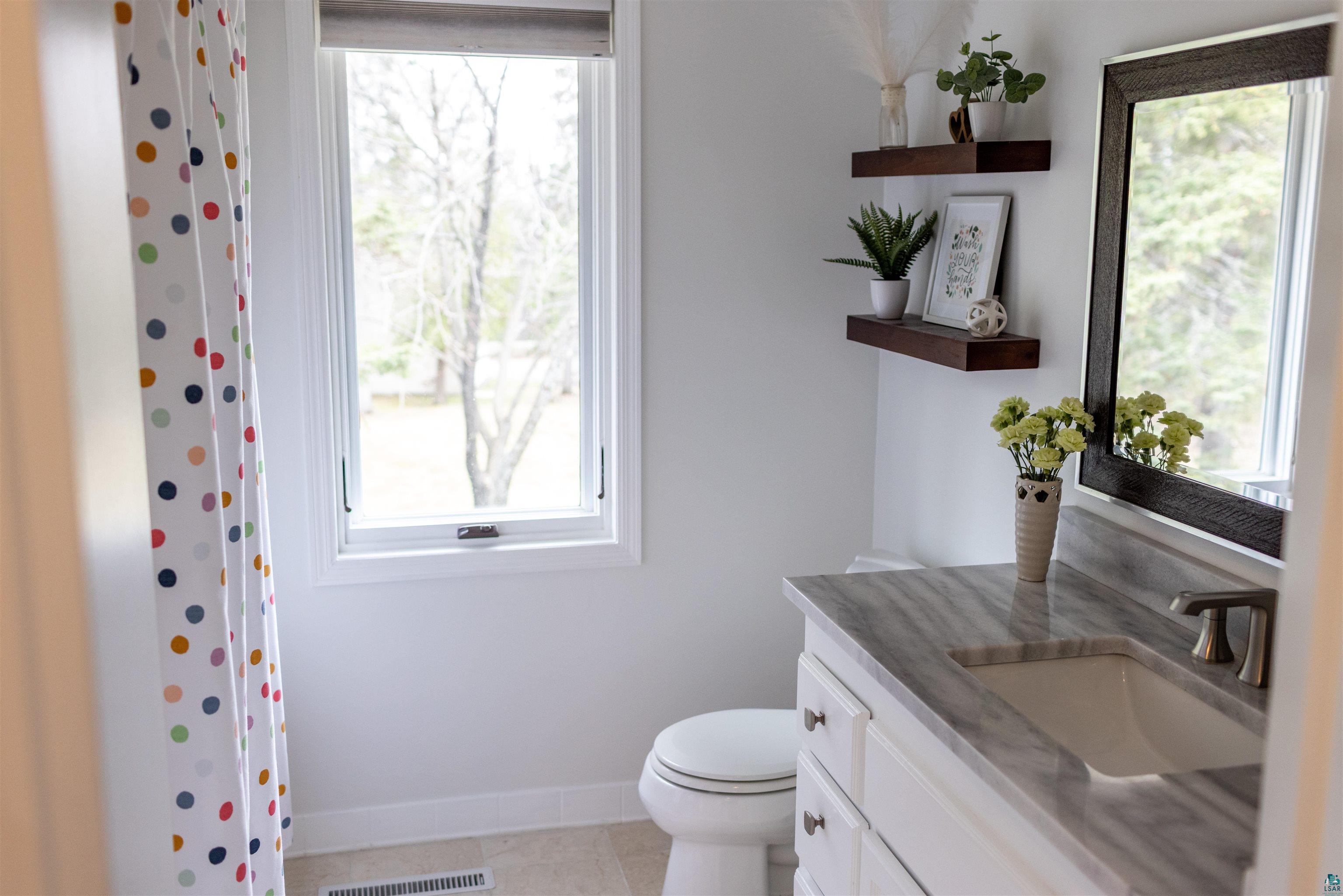 3704 Greysolon Road Duluth, MN 55804 - Photo 18 of 51 Bathroom featuring a single-pane window, single vanity with a stone countertop, undermount sink, and a framed mirror