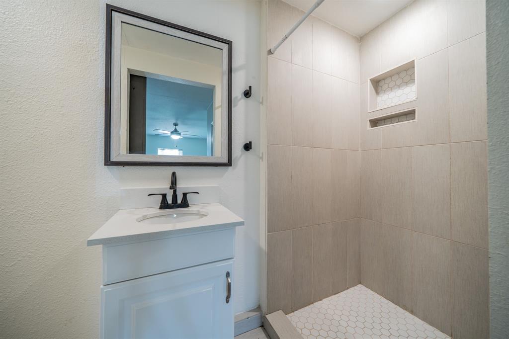 11528 Sinclair Avenue Dallas, TX 75218 - Photo 9 of 16 Bathroom featuring a white vanity with an integrated sink and matte black faucet, a framed mirror, and a tiled shower with recessed niches