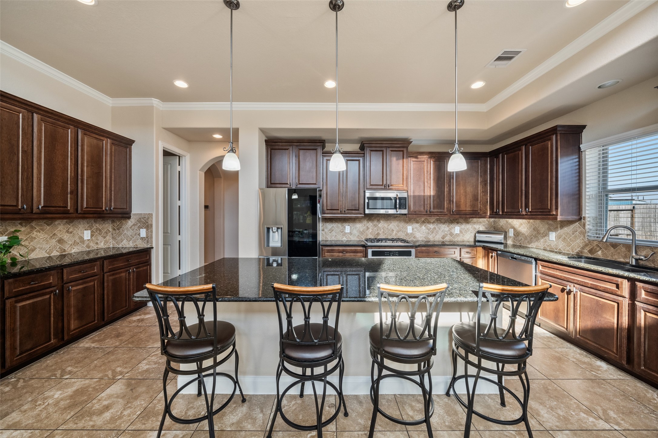 4747 Abercorn Street Rosharon, TX 77583 - Photo 17 of 46 This spacious kitchen features elegant dark wood cabinets, granite countertops, and a large central island with seating for four. It includes modern stainless steel appliances and ample natural light, creating a warm and inviting atmosphere.