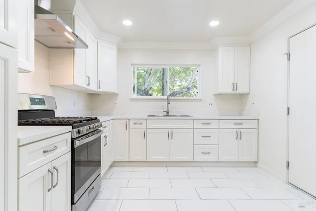 a kitchen with white cabinets appliances a sink and a window