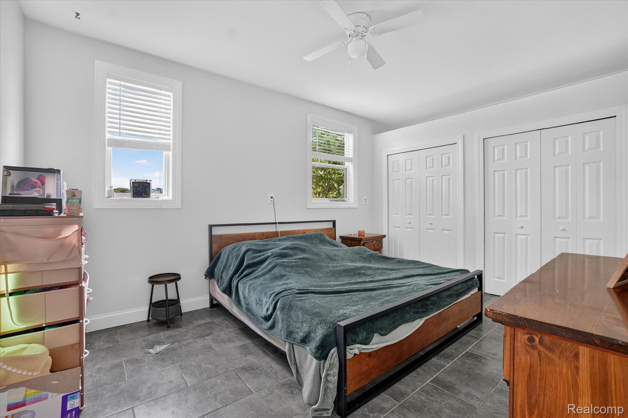 6524 Kelly Road Flushing, MI 48433 - Photo 24 of 47 Room featuring gray tile flooring, two windows with white blinds, a white ceiling fan, and two white bi-fold closet doors