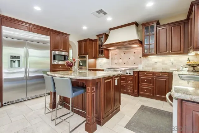 a kitchen with stainless steel appliances granite countertop a stove top oven a sink dishwasher and a refrigerator with wooden cabinets