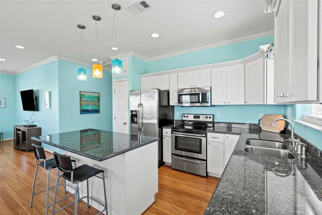 a kitchen with stainless steel appliances granite countertop a stove top oven a sink dishwasher a dining table and chairs with wooden floor