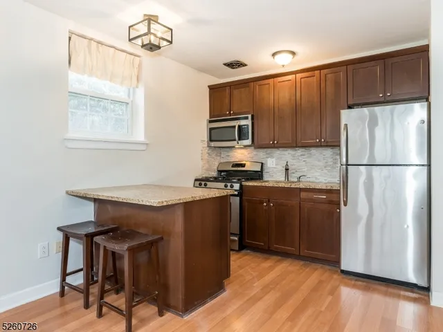 a kitchen with stainless steel appliances granite countertop a refrigerator a stove a sink dishwasher and wooden cabinets with wooden floor