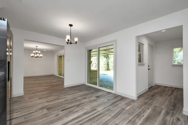 an empty room with wooden floor chandelier and windows