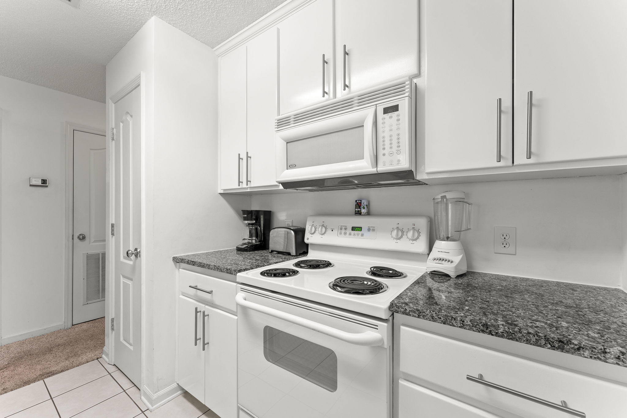 17462 Front Beach Road, Unit 77H Panama City Beach, FL 32413 - Photo 11 of 28 a kitchen with white cabinets and white appliances