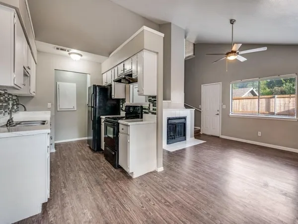 a kitchen with stainless steel appliances a stove top oven a sink dishwasher a refrigerator and a dining table with wooden floor