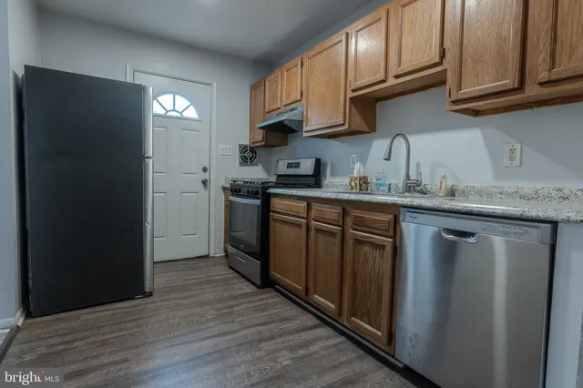 a kitchen with stainless steel appliances granite countertop a refrigerator a sink dishwasher and wooden cabinets with wooden floor