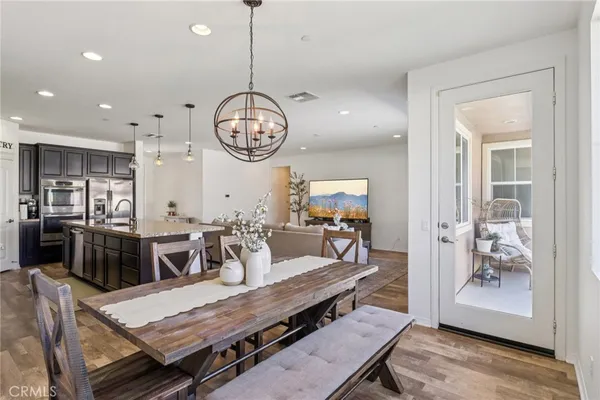 a kitchen with stainless steel appliances granite countertop a refrigerator a stove a sink a dining table and chairs with wooden floor