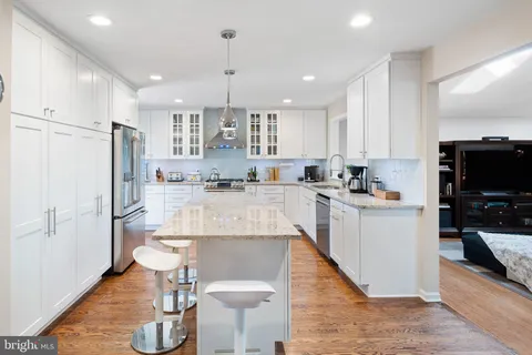 a kitchen with stainless steel appliances kitchen island granite countertop a refrigerator a stove a sink a dining table and chairs with wooden floor